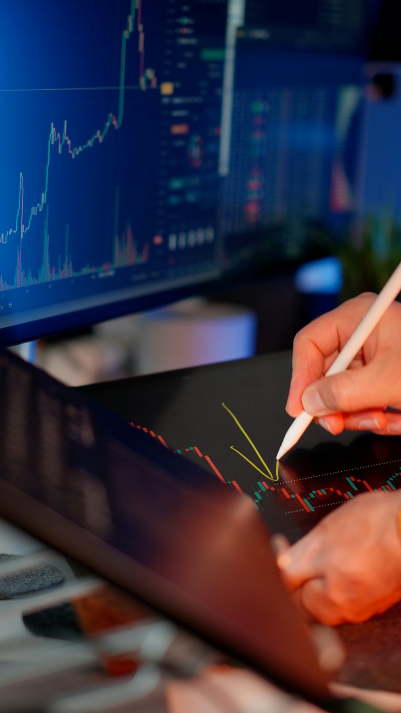 Hands using a stylus on a tablet with financial charts.